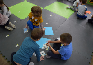 Dzieci siedzą na macie w grupkach trzyosobowych, układają puzzle do bajki "Jarzębinka"